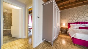 A bedroom with a wooden ceiling, a white wardrobe, a bed with pink bedding, and a bathroom visible through an open door. - The Baroness Apartment   Lady Capulet (Verona)