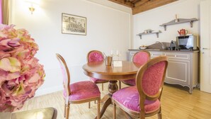 A dining area with a wooden table and chairs, a vase of flowers, and a kitchen in the background. - The Baroness Apartment   Lady Capulet (Verona)