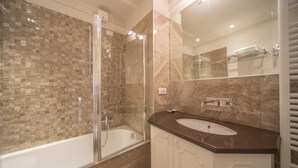 A modern bathroom with a glass-enclosed shower, a bathtub, and a vanity with a sink. - The Baroness Apartment   Lady Capulet (Verona)