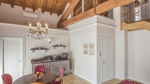 A spacious living room with a high wooden ceiling, a dining area with pink upholstered chairs, and a kitchen in the background.