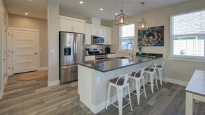 Una cocina moderna con armarios blancos, electrodomésticos de acero inoxidable y una isla central con taburetes de bar.