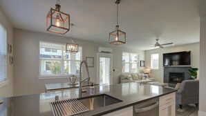 Una cocina moderna con una isla central, luces colgantes y una chimenea empotrada.