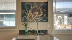 Una cocina con una isla de acero inoxidable, un cuadro de un pulpo en la pared y un ventanal con persianas.