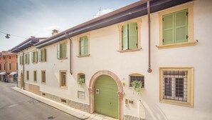 Un bâtiment avec une porte verte, de nombreuses fenêtres dotées de volets verts et un petit balcon orné de plantes.