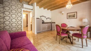 Un salon chaleureux avec un canapé violet, une table à manger en bois et quatre chaises, et une cuisine en arrière-plan.