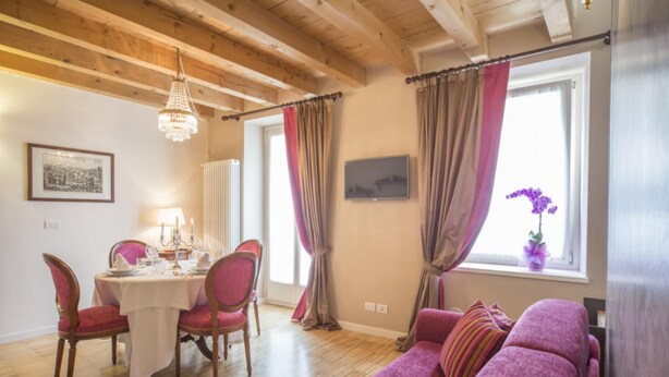 Une pièce avec un plafond en bois, une table à manger entourée de chaises rouges, un canapé et une fenêtre avec des rideaux.