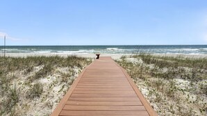 Ein hölzerner Steg führt zum Strand, im Hintergrund Dünen und Meer.