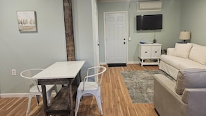 A living room with a dining table, white chairs, a sofa, a TV, and a lamp. - The Wee Nook, just 3 miles from Carver Landing! (Piercetown)