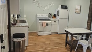 A compact kitchen with white appliances, a wooden floor, and a dining area with a table and chairs. - The Wee Nook, just 3 miles from Carver Landing! (Piercetown)
