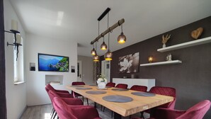 Et moderne spiseområde med et træbord, røde polstrede stole, hængende lamper og et fjernsyn på væggen.
