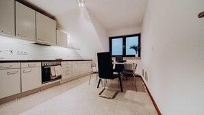 Une cuisine avec des meubles blancs, une chaise noire et une fenêtre donnant sur le ciel.
