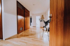 Un couloir avec un plancher en bois, une plante en pot et une porte blanche.