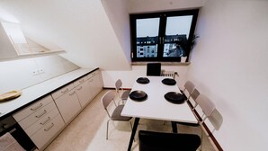 Une cuisine de taille réduite comprenant une table à manger, des chaises et une fenêtre donnant sur un paysage urbain.