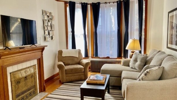 Un salon avec une cheminée, un canapé, un fauteuil, une télévision et une lampe.
