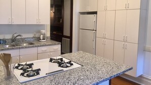 Une cuisine avec des armoires blanches, un comptoir en granit, une cuisinière à gaz et un réfrigérateur.