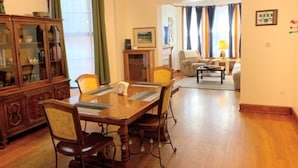 Un coin repas avec une table et des chaises en bois, un meuble avec des portes en verre, et une vue sur un salon comprenant un canapé et une lampe.