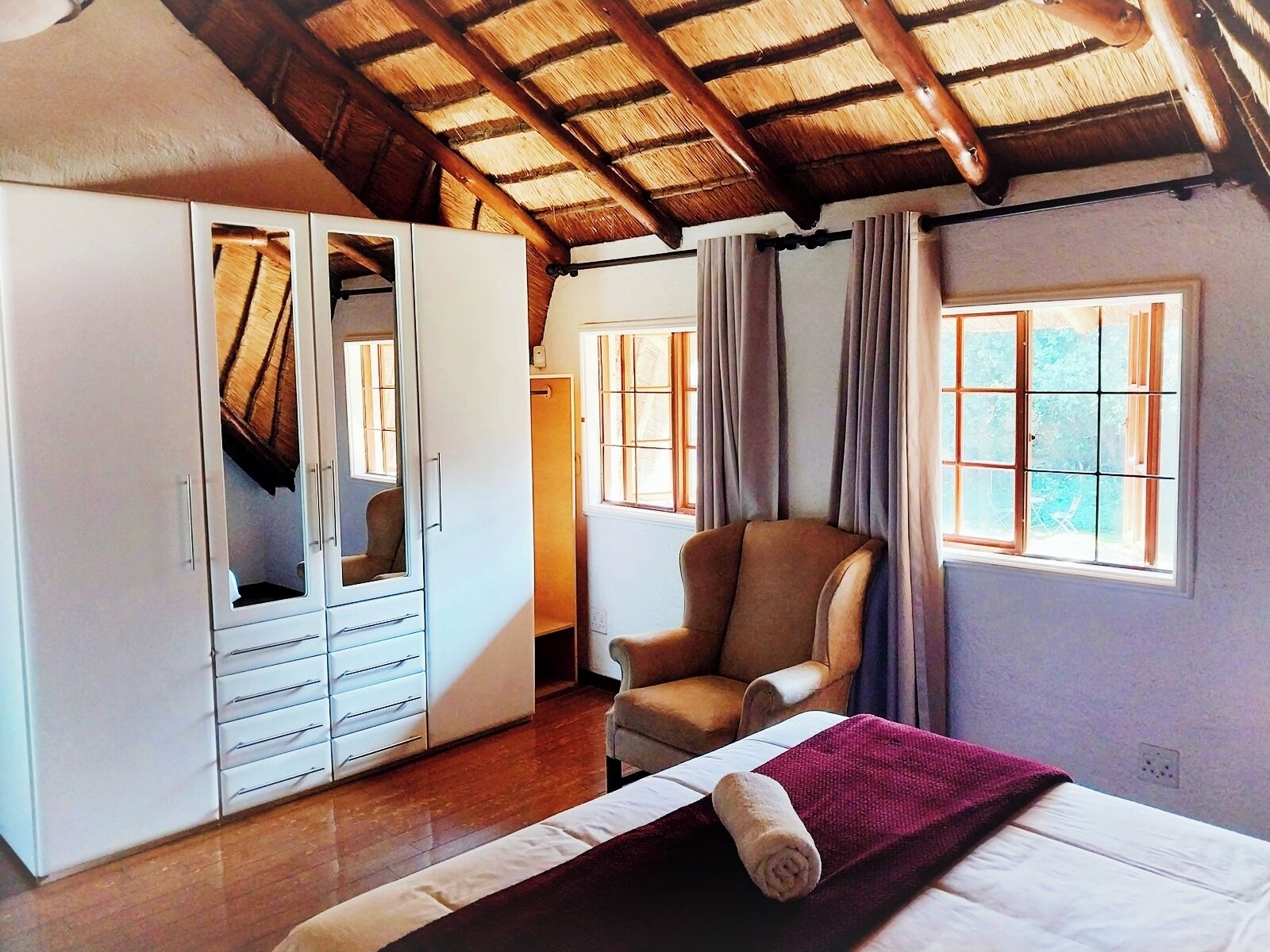 Un dormitorio con cama, una silla, armario y ventana con cortinas.