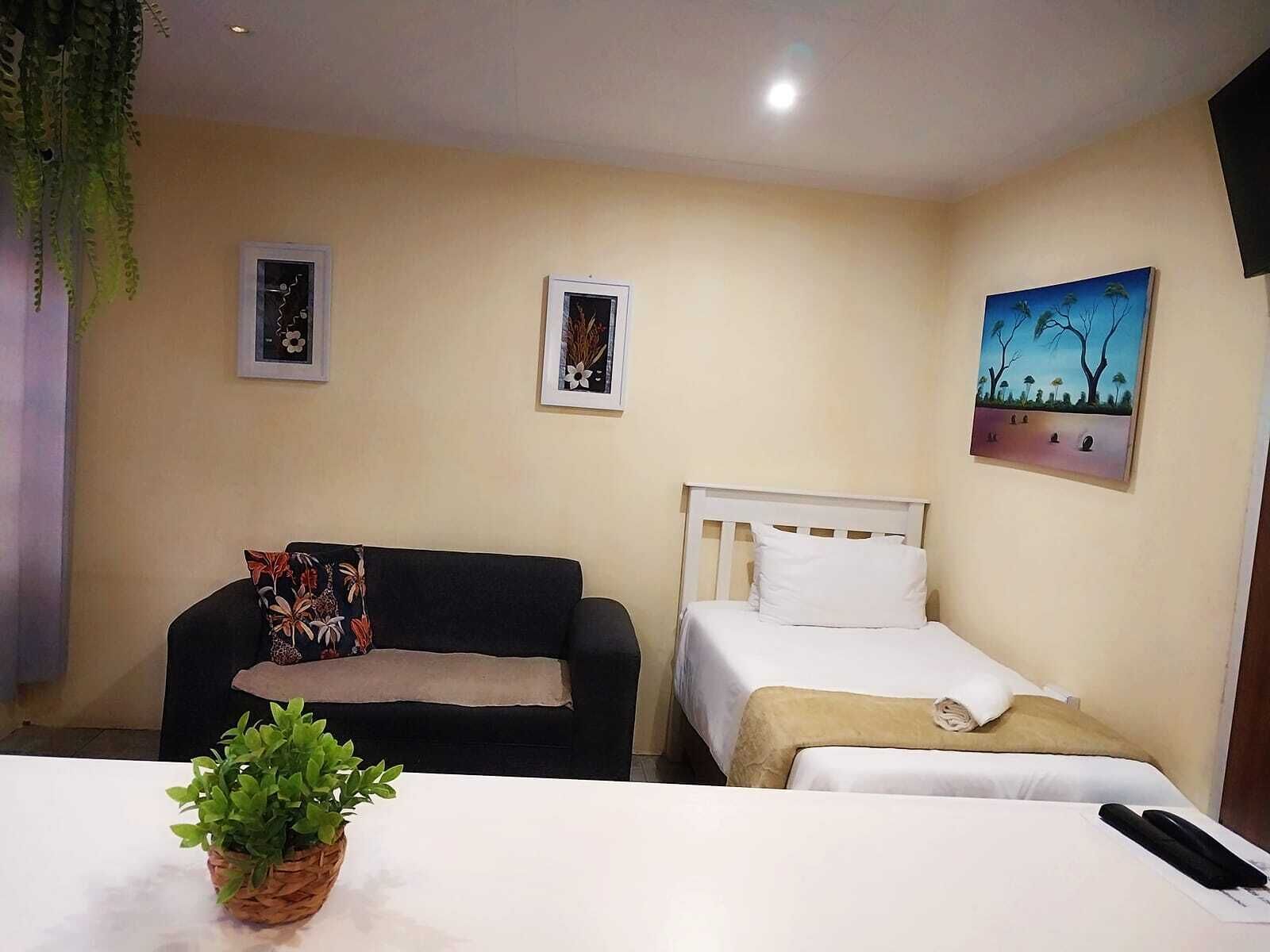 Une pièce comprenant un lit, un canapé, une petite table avec une plante et deux tableaux encadrés accrochés au mur.