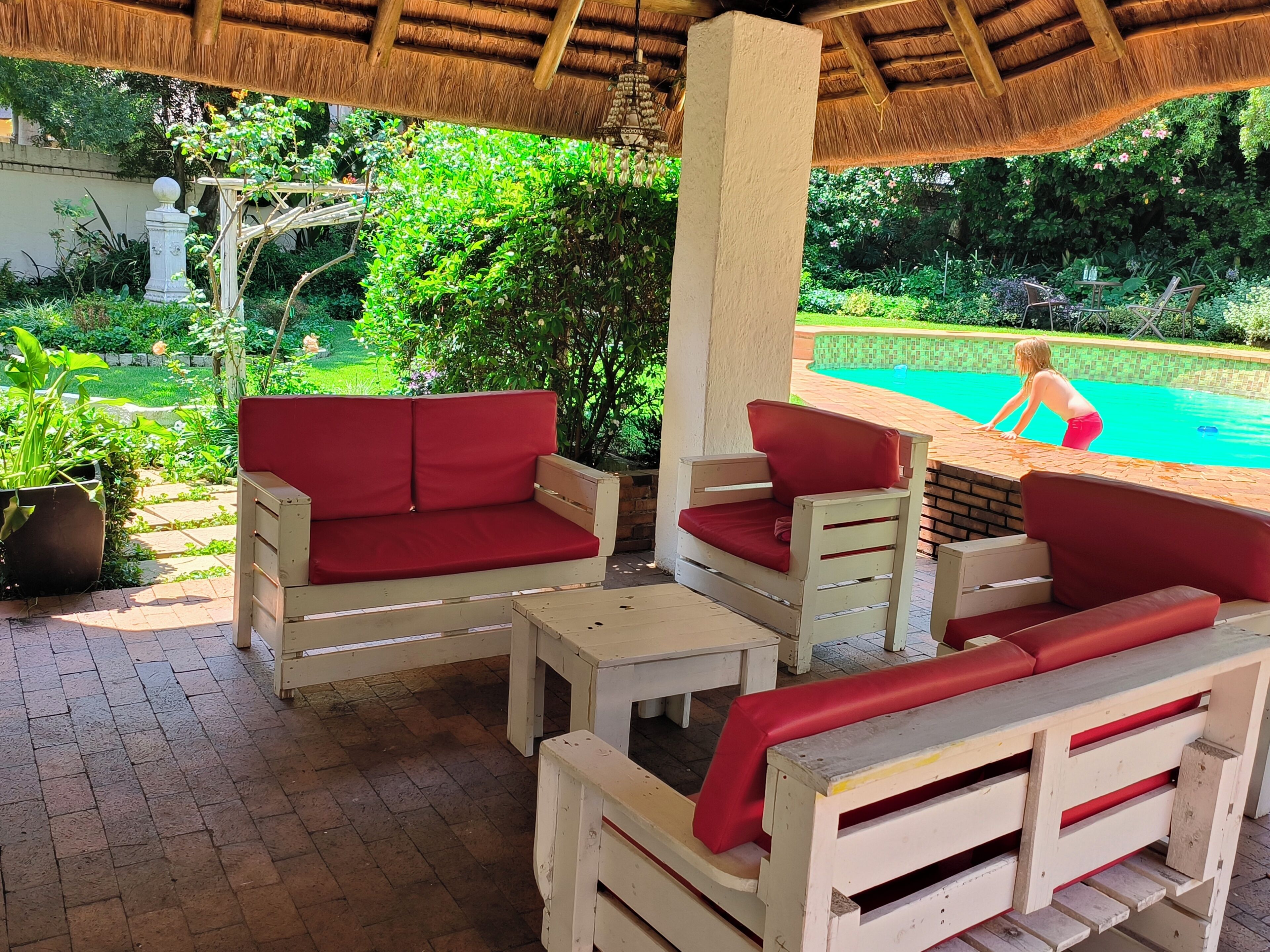 A covered outdoor seating area with wooden furniture and a pool in the background.