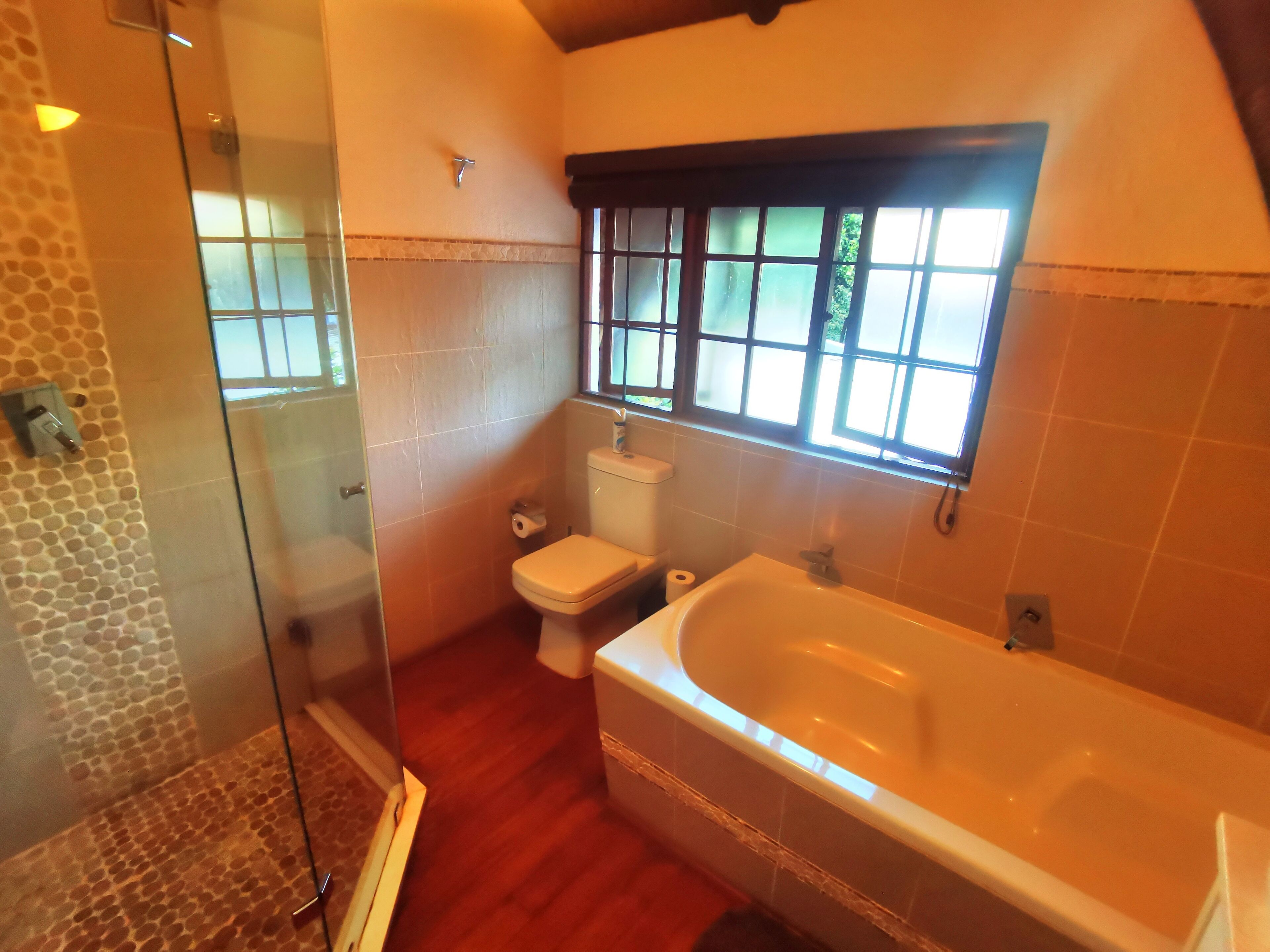 A bathroom with a glass shower enclosure, a toilet, a bathtub, and a window with frosted glass panes.