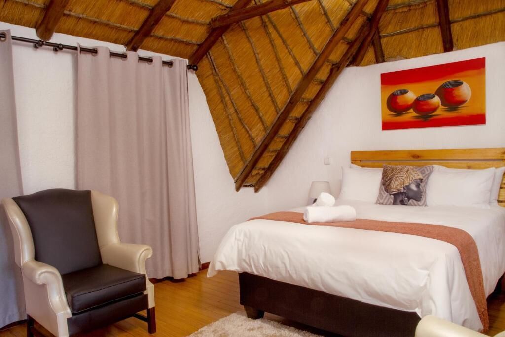 Ein Schlafzimmer mit einem Bett, einem Sessel, einem Gemälde und einer Holzbalkendecke.