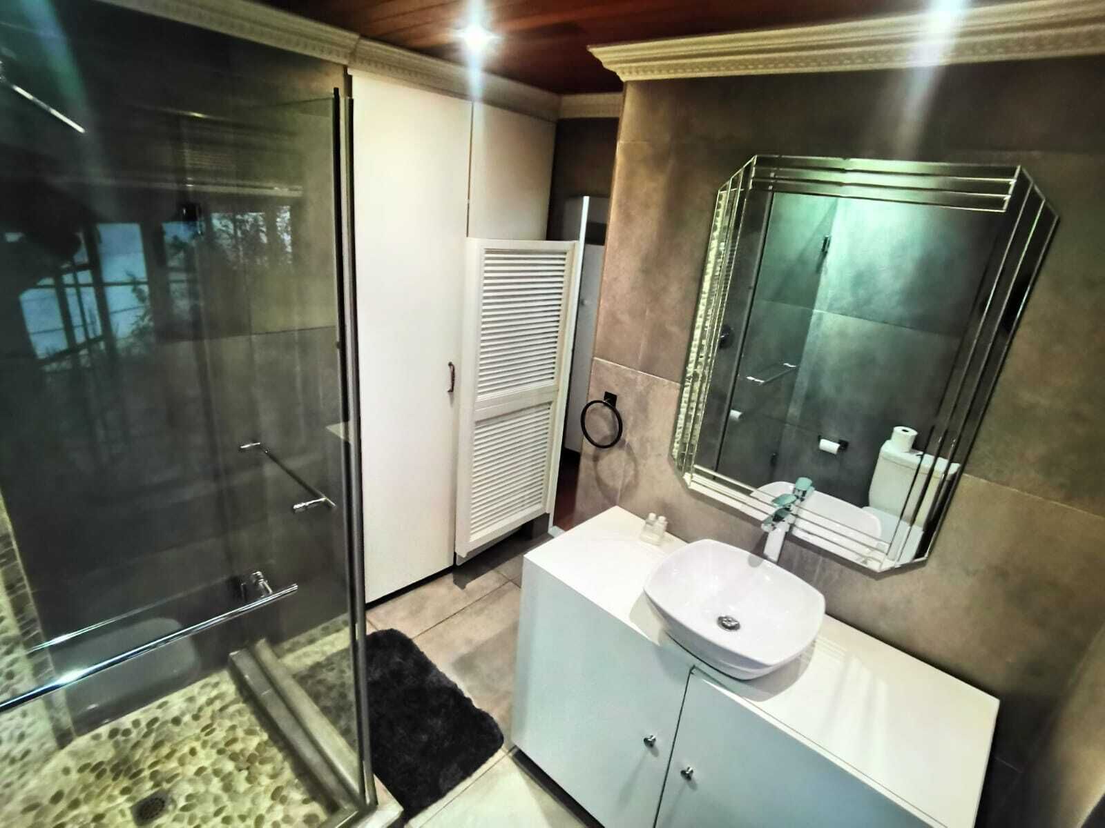 A modern bathroom with a glass shower enclosure, a white vanity with a sink, and a large mirror.