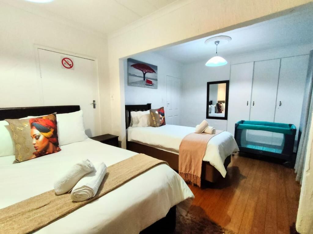 Una habitación de hotel con dos camas, piso de madera, un espejo y una lámpara en el techo.