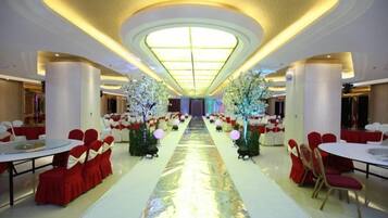 Un salón de banquetes con mesas redondas y sillas, un pasillo central y árboles decorativos.