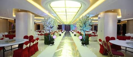 A banquet hall with round tables and chairs, a central aisle, and decorative trees.