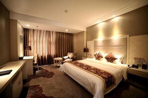 A hotel room with a large bed, a desk, a chair, a lamp, and a curtain.
