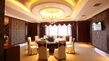 A formal dining room with a chandelier, round table, and chairs with red sashes.