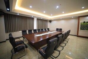 Un salón de conferencias con una larga mesa, sillas negras y vistas al exterior a través de una ventana.
