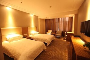 A hotel room with two beds, a desk, a chair, a TV, and a large window with curtains.