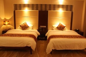 A hotel room with two beds, each with a headboard, bedside tables, and lamps.