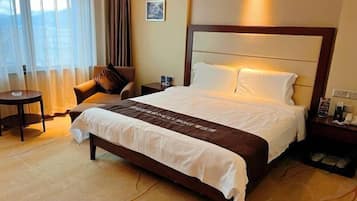 Habitación de hotel con cama, sillón, mesita de noche y ventana con cortinas.
