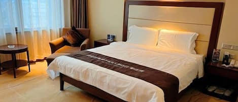 A hotel room with a bed, a chair, a nightstand, and a window with curtains.