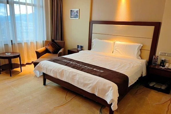 A hotel room with a bed, a chair, a nightstand, and a window with curtains. - Xintianfu International Hotel (Wangqing)