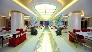 Una sala da banchetti con tavoli rotondi e sedie, un corridoio centrale e composizioni floreali decorative.