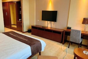 A hotel room with a bed, a TV mounted on the wall, a desk with a chair, and a wardrobe. - Xintianfu International Hotel (Wangqing)