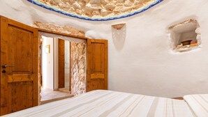 A room with a bed, wooden doors, a small window, and a tiled ceiling.