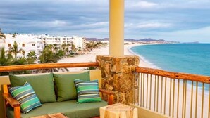 Un balcón con banca de madera, un pilar de piedra y vistas a una playa y edificios.