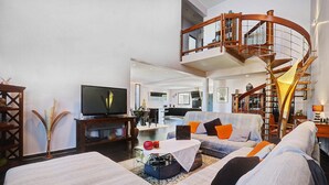 A spacious living area with a modern staircase, a flat-screen TV, and comfortable seating. - La Villa des Mainates - Jacuzzi et vue mer (Le Tampon)