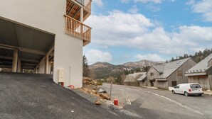 A parking area with a white van, a building with a balcony, and a mountainous backdrop.
