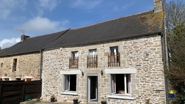 Un bâtiment en pierre avec un toit en pente, deux fenêtres avec volets et une porte.