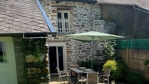 Une maison en pierre dotée d’un patio comprenant une table, des chaises, un parasol et une porte.