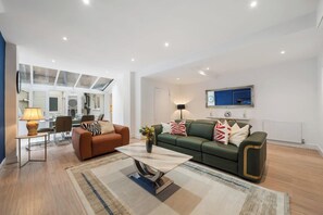 Een moderne woonkamer met een bank, fauteuil, salontafel en een aan de muur bevestigde televisie.