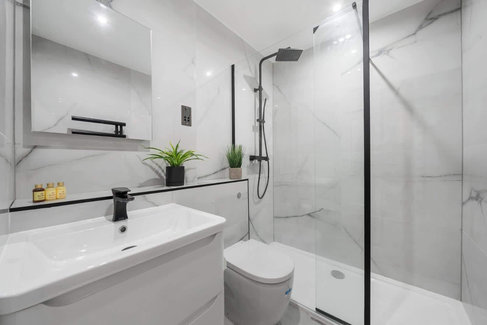 A modern bathroom with a white marble sink, a glass shower enclosure, and a small potted plant on the vanity.