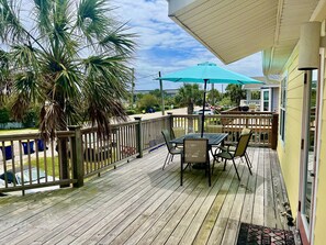 A wooden deck with a table and chairs, a palm tree, and a blue umbrella.