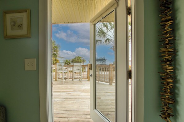 A view through a glass door into a wooden deck area with outdoor furniture and a wooden fence.