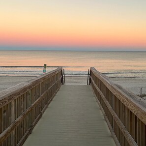 A wooden boardwalk leading to a beach with a calm sea and a sunset sky.